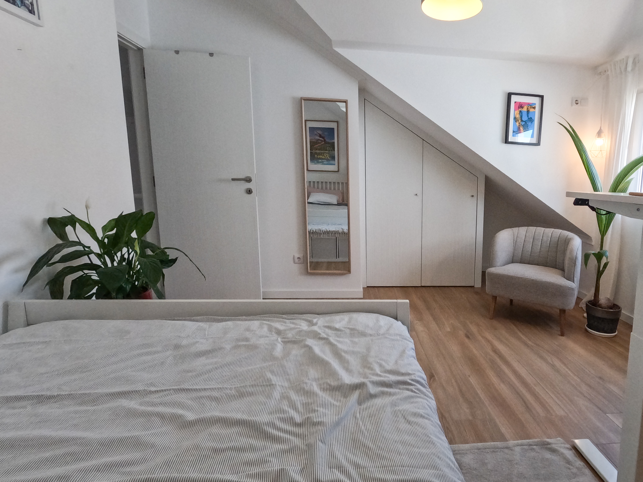 Bedroom with comfortable bed, wardrobe, reading chair, and surf art