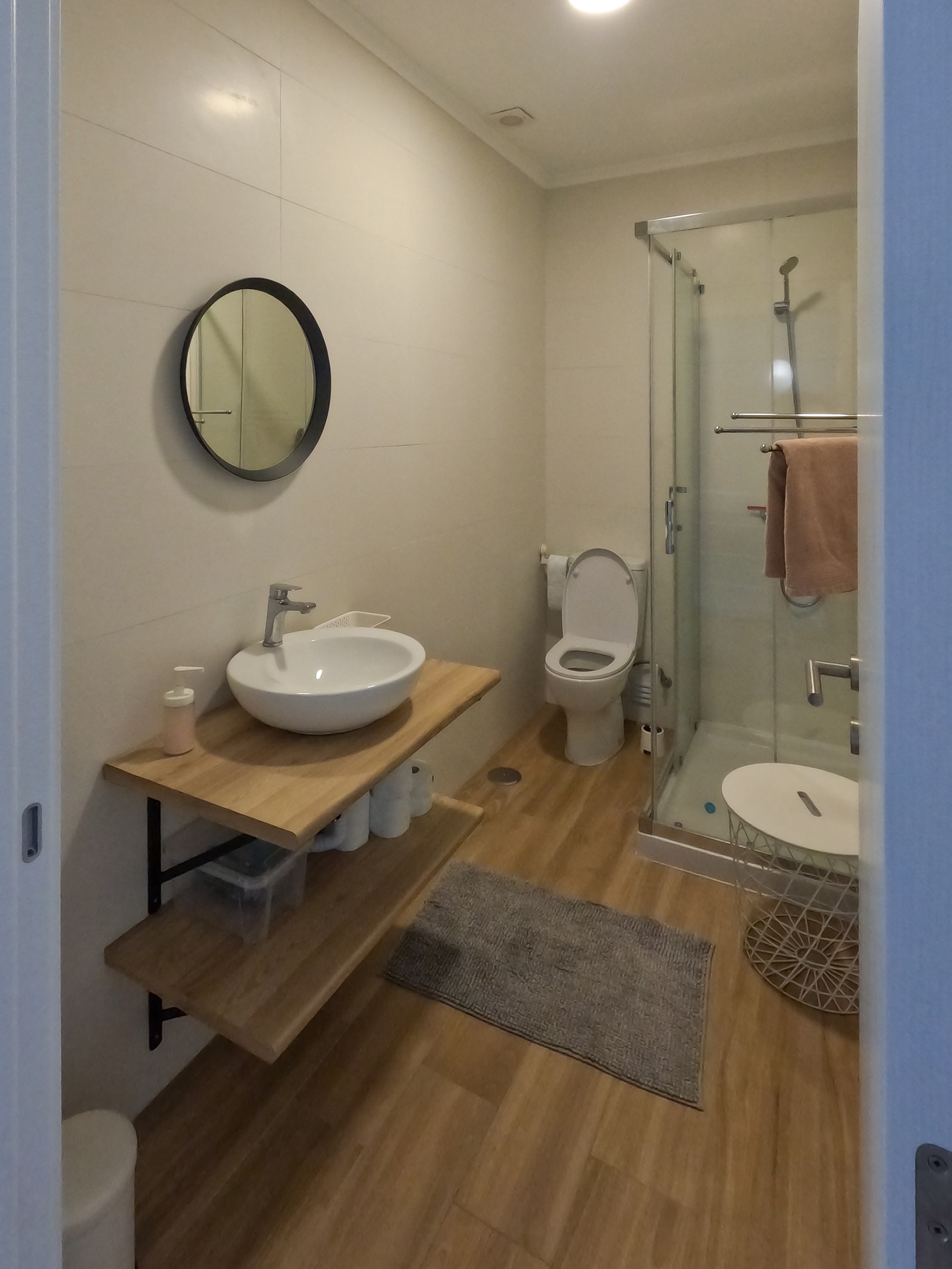 Modern private bathroom with wood vanity, round mirror, and glass shower